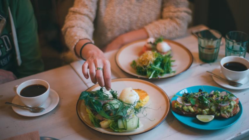 Crop anonymous female eating healthy meal served on plate with coffee on table in restaurant