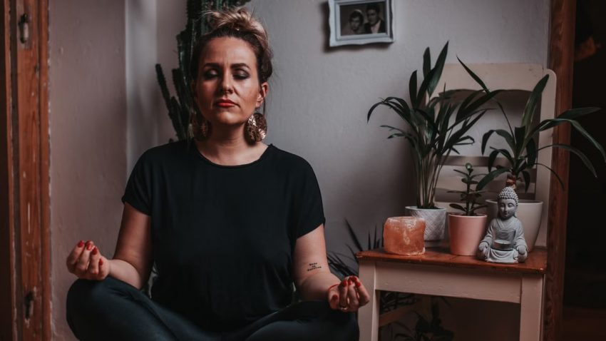 Peaceful female in black clothes and stylish earring meditating during yoga session at home