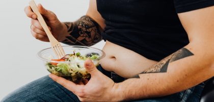 A tattooed individual holding a fresh salad, symbolizing healthy lifestyle and fitness motivation.