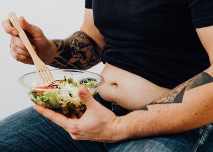 A tattooed individual holding a fresh salad, symbolizing healthy lifestyle and fitness motivation.