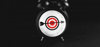 Black alarm clock with target on black background.