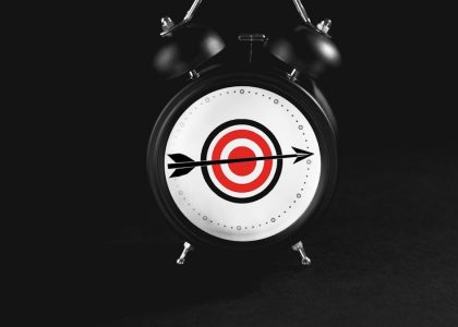 Black alarm clock with target on black background.